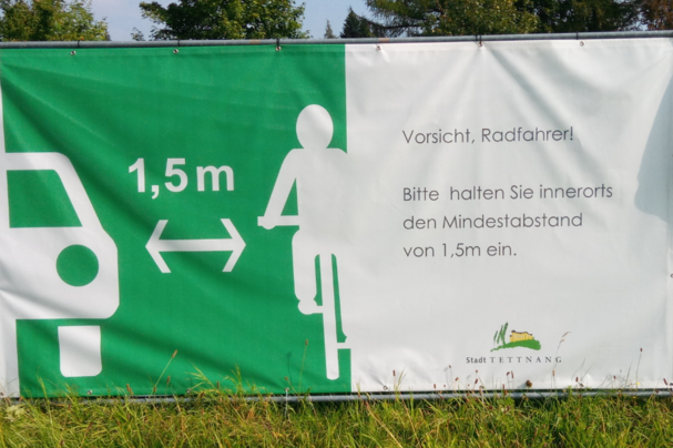 Abbildung 2: Infoplakat an einem Bauzaun das auf den gesetzlichen Mindestabstand zu Fahrradfahrern beim Überholvorgang hinweist. 