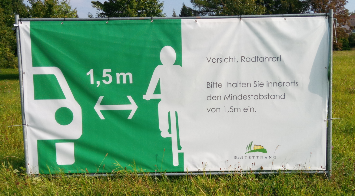 Abbildung 2: Infoplakat an einem Bauzaun das auf den gesetzlichen Mindestabstand zu Fahrradfahrern beim Überholvorgang hinweist. 